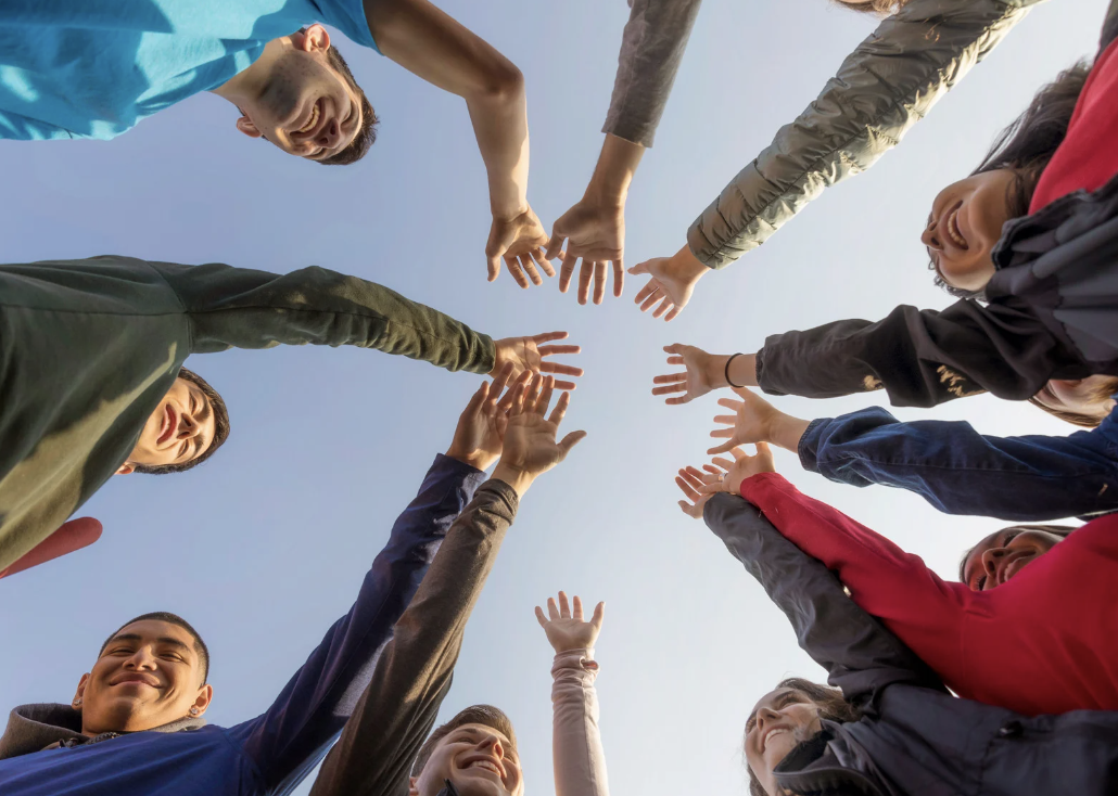 Group of diverse people raising their hands in a circle, illustrating community building and its positive impact on mental health.